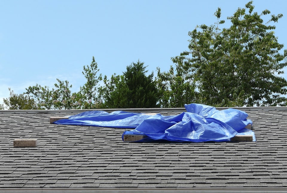 A blue plastic tarp over a roof leak provides temporary protection from further damage to a residence; roof storm damage