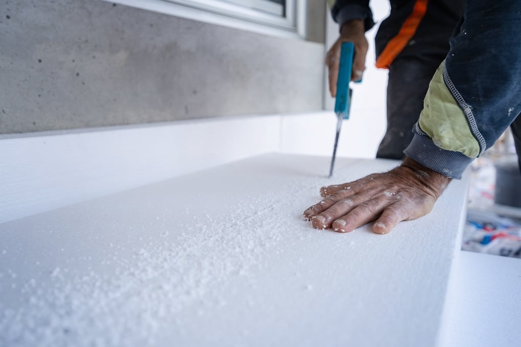 Roofer using the hand saw to cut the polystyrene insulation panel for flat roof insulation