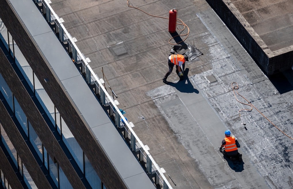 Roofing contractors repairing damaged flat roof on commercial building