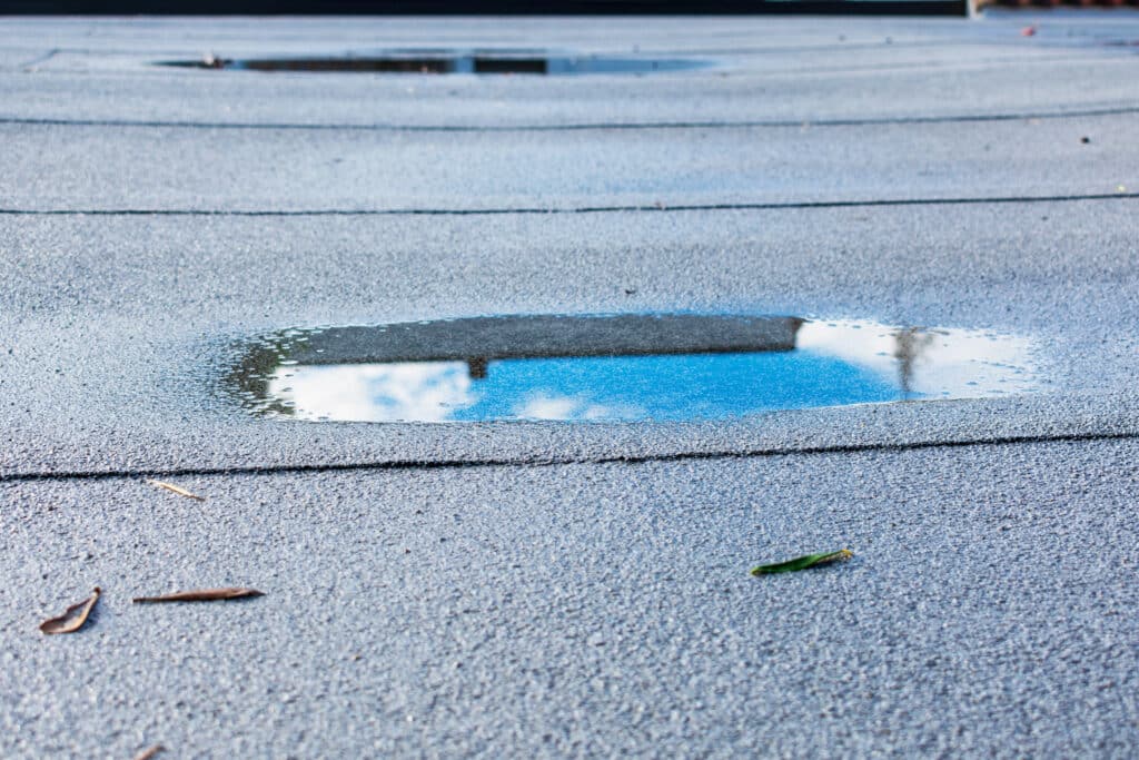 Ponding rainwater on flat roof after rain is result of drainage problem. Roof leaking, settling, sagging, framing issues, rotten or saturated sheathing.