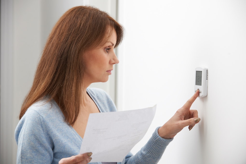 Woman Turning down thermostat because of high energy bills due to poor roof ventilation