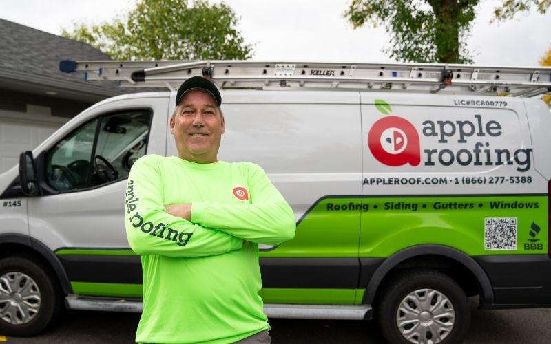 Apple Roofing consultant in front of a work van parked outside a home